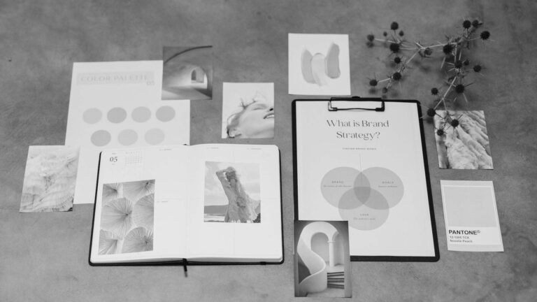 Flat lay of brand strategy documents, color palettes, Pantone swatch, and photos arranged on a workspace surface.