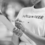 Volunteer wearing a labeled shirt, holding a clipboard and pen, capturing information.