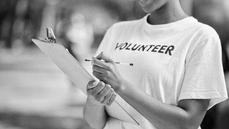 Volunteer wearing a labeled shirt, holding a clipboard and pen, capturing information.