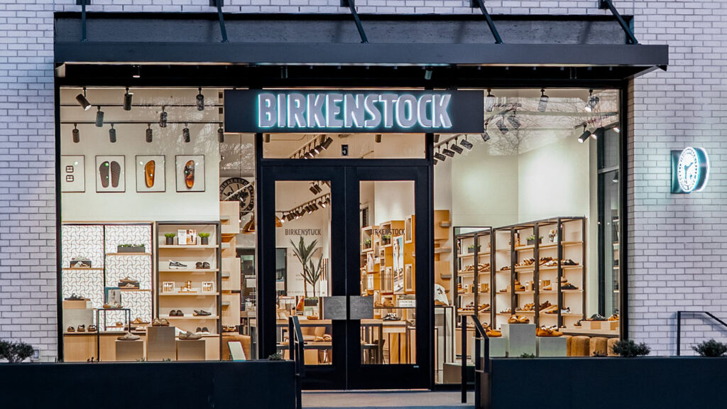 Exterior view of Birkenstock store with illuminated signage and shoe displays visible through glass windows.